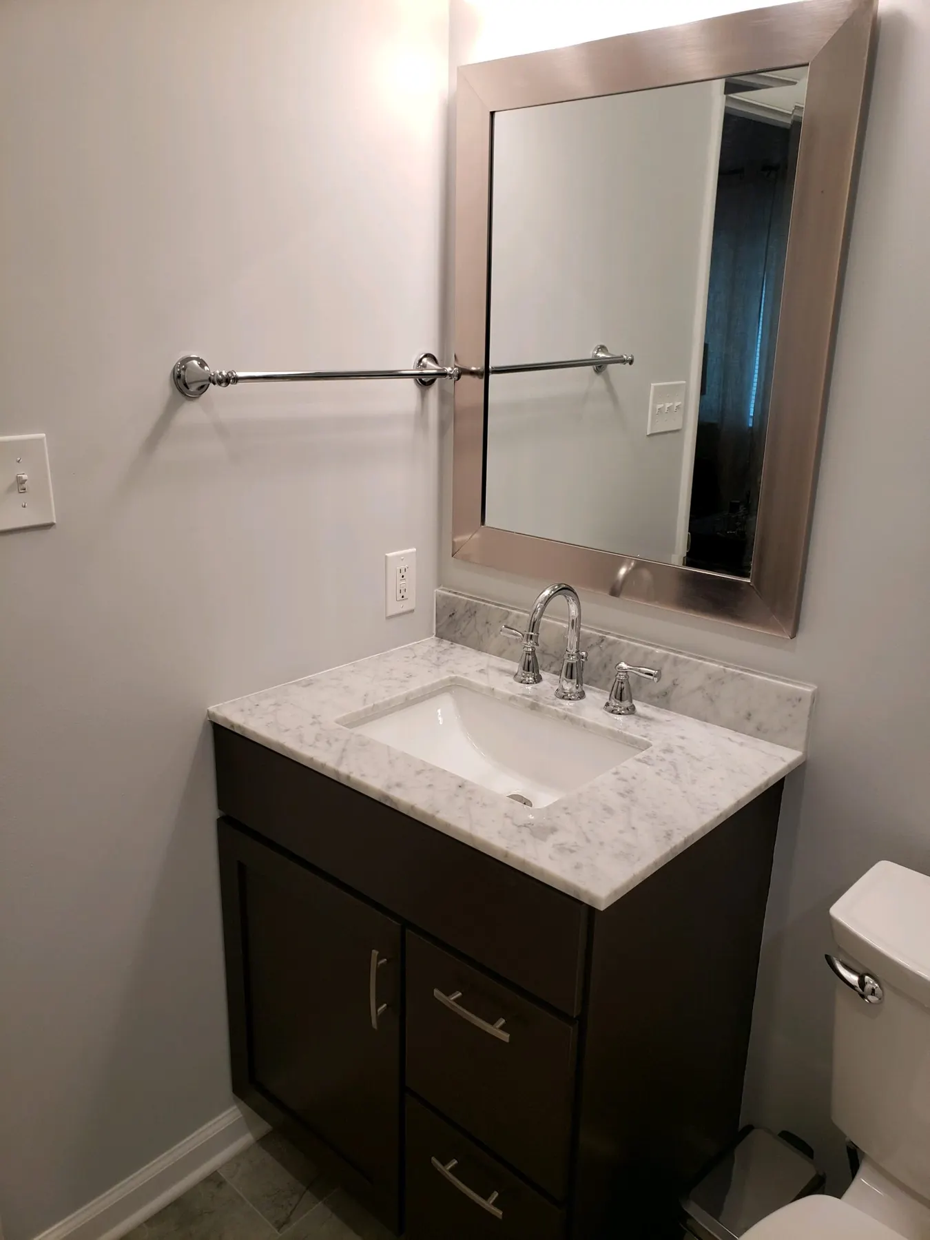 Dark wood vanity with marble top and framed mirror.