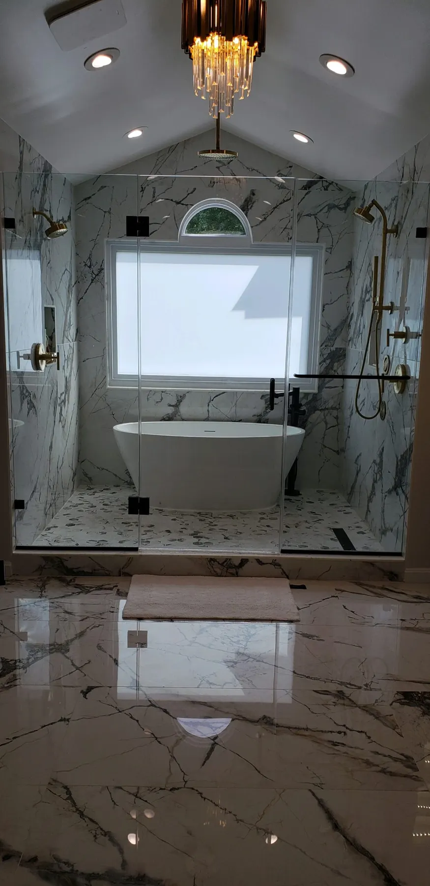 Freestanding tub in a marble wet room with black-framed shower glass.