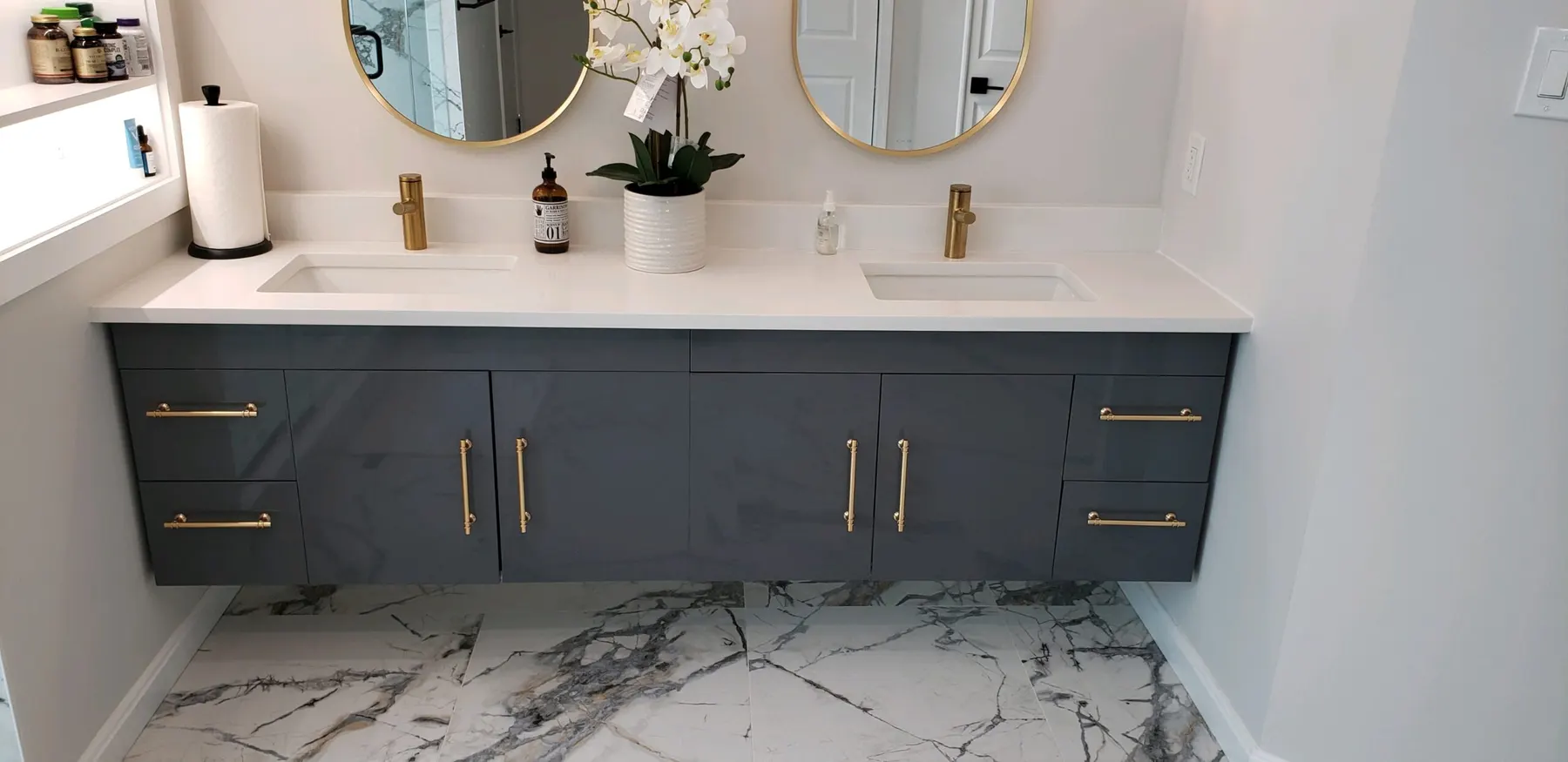 Navy vanity wall with gold hardware over marble-look tile floor.