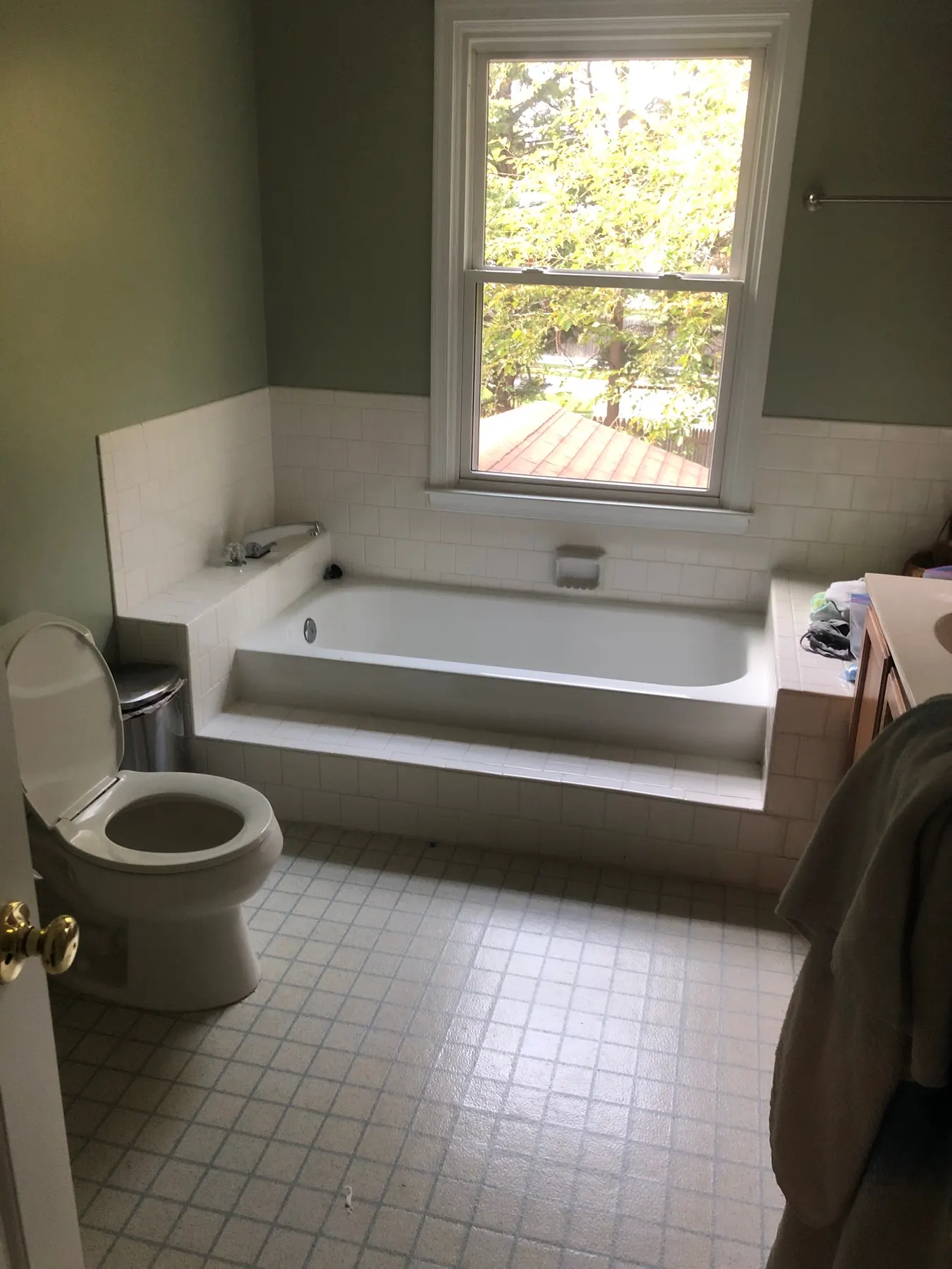 Old beige tub and toilet by a window before renovation.