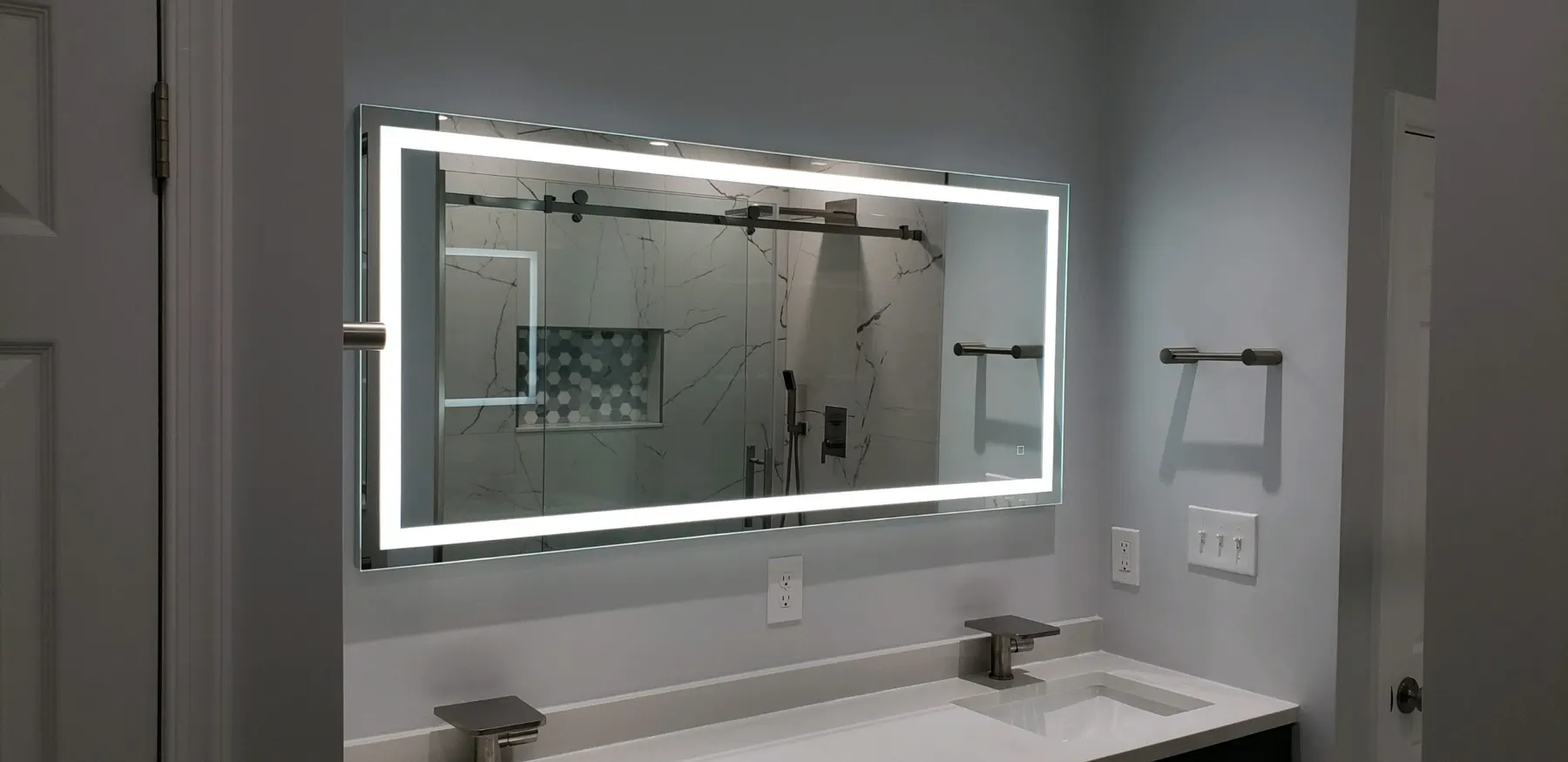 LED-framed vanity mirror reflecting a new marble shower.
