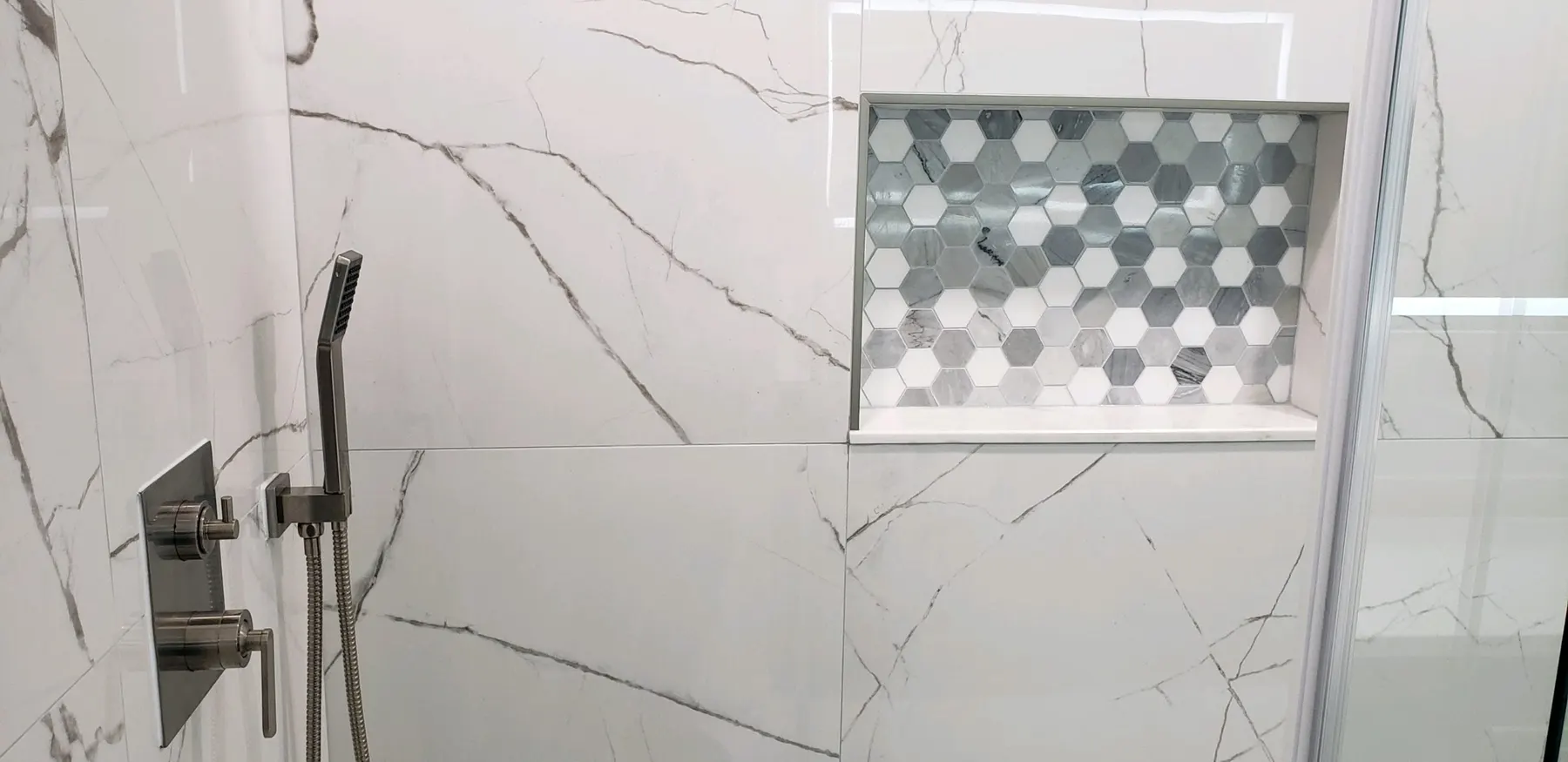 Marble shower wall with a hexagon-tile niche.