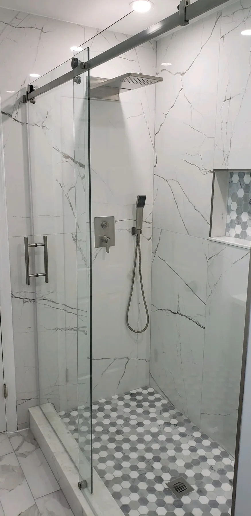 Frameless glass shower door on a marble-tiled shower.