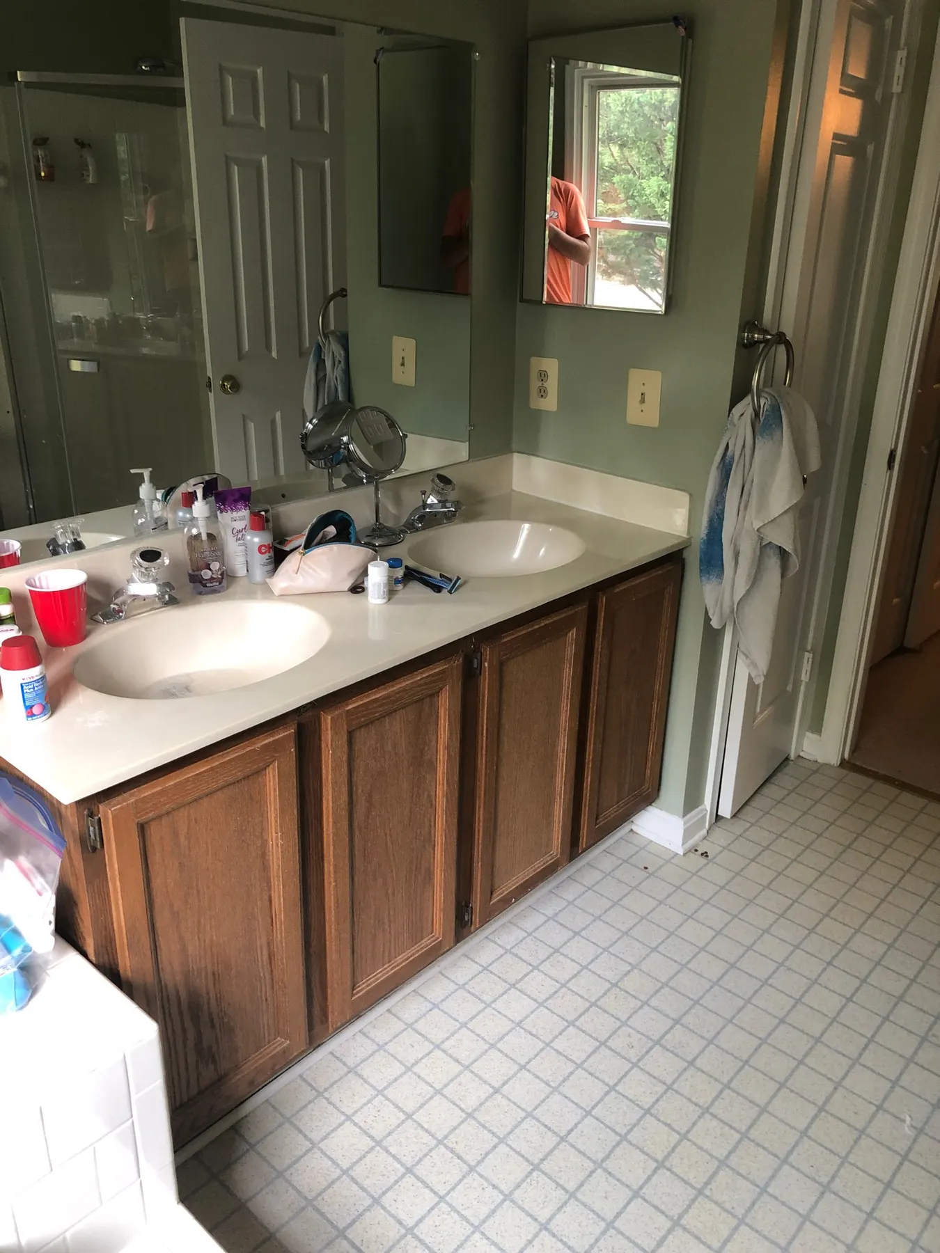 Before: dated oak double vanity with green walls and vinyl tile floor.